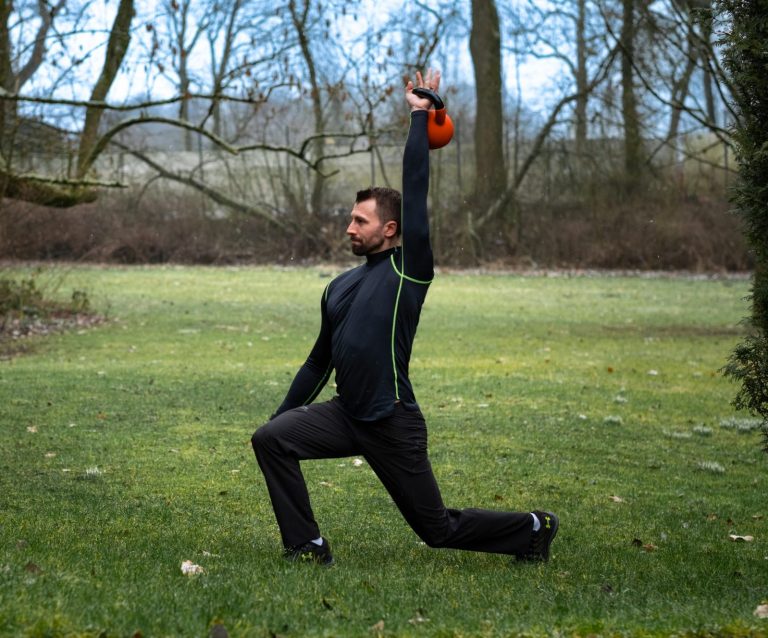 Outdoor Fitness Mann führt eine Kettlebell-Übung im Ausfallschritt auf einer Wiese aus.
